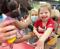 A little girl with blonde hair and a big smile on her face playing with an interactive doll using a button switch