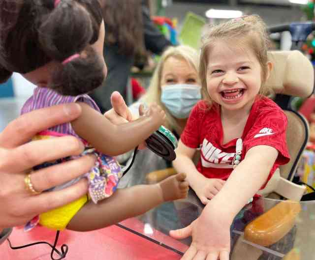 A little girl with blonde hair and a big smile on her face playing with an interactive doll using a button switch