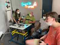 three individuals playing video games, another person is standing near a neon Powered by AbleGamers sign. The photo was taken at Ability KC. Resources for People With Disabilities
