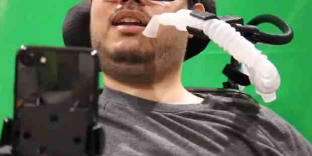 Milan in his wheelchair, waring a gray shit and dark rimmed glasses.