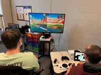 two people playing a video game on a large screen at the front of the room. Photo provided by Ability KC.