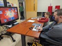 photo provided by Powered by AbleGamers partner Easterseals Iowa. two people playing a video game together, one a young boy the other a young man using an Xbox adaptive controller