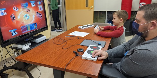 photo provided by Powered by AbleGamers partner Easterseals Iowa. two people playing a video game together, one a young boy the other a young man using an Xbox adaptive controller