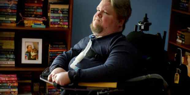 Steven Spohn, AbleGamers Chief Operating Officer sitting in front of a bookshelf full of books