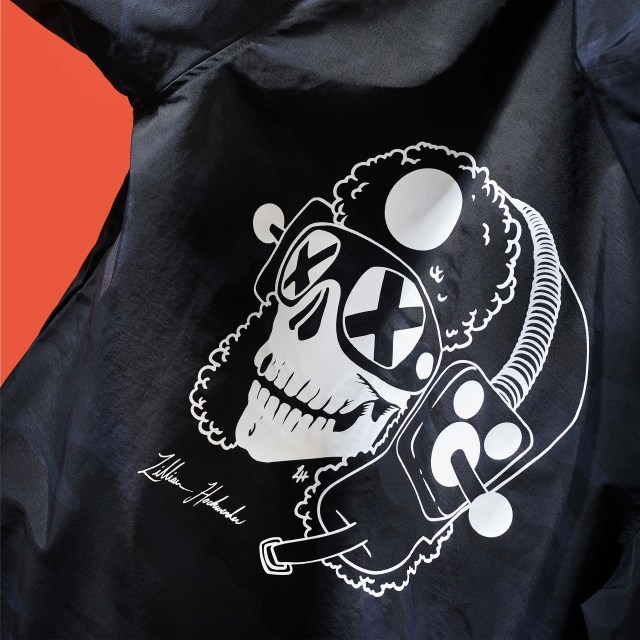 A jacket with the Voodo Ranger mascot wearing stylized glasses and a sylized hat that features 2 ablegamers joysticks as earmuffs.