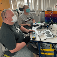 two individuals playing a video game, being social, and not isolated, using several different switches and adaptive controllers