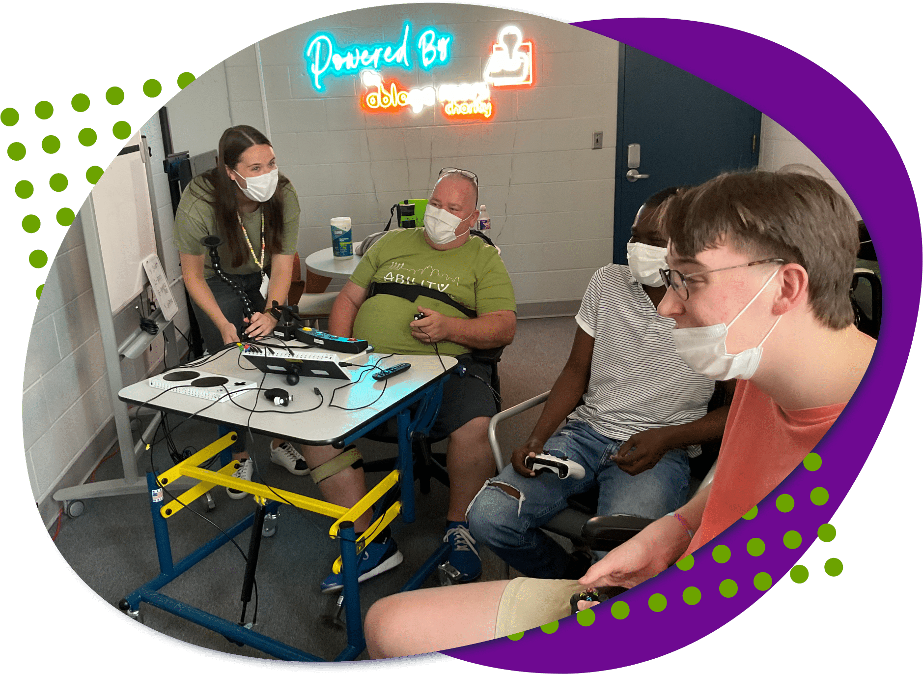 AbKC an image of four individuals, one standing leaning over and the other three individuals are sitting playing a video game together.