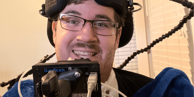 Dylan W a dark haired guy with glasses. His quadstick, a controller you use your mouth, is in front of him.