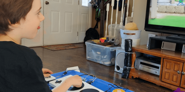 A photo of Elliott playing a video game with his adaptive gaming controller setup