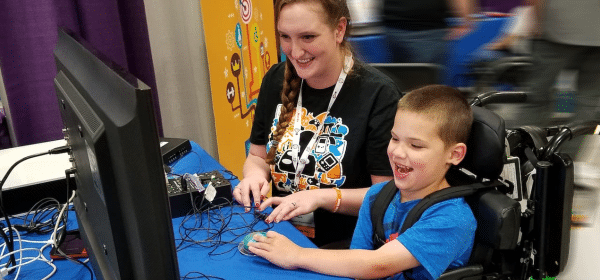 Peer Counselor Jessi playing video games with a young boy in a wheel chair, both are smiling and having fun