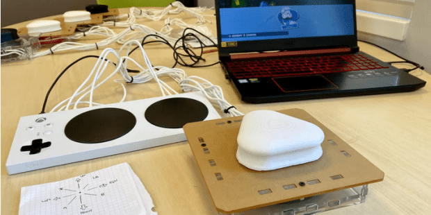 A table with an open laptop in the center wired to an Xbox Adaptive Controller and the controller developed by UPEI students wired to the Xbox Adaptive Controller