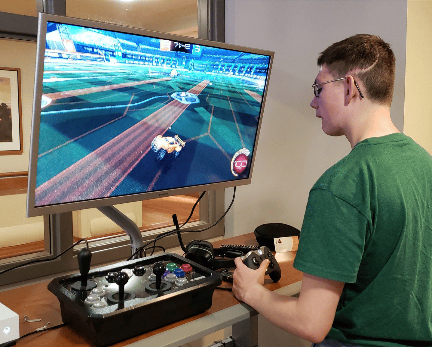 a young man holding a game controller in one hand playing a video game a large monitor in front of him