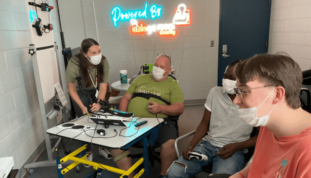 whats the impact three men playing video games together using several adaptive gaming devices a young woman who is an occupational therapist is watching photo provided by Ability KC a Powered by AbleGamers partner